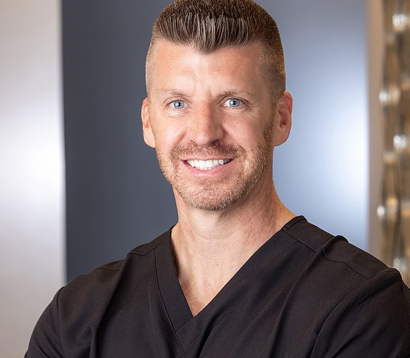 Smiling man in medical scrubs with short hair.