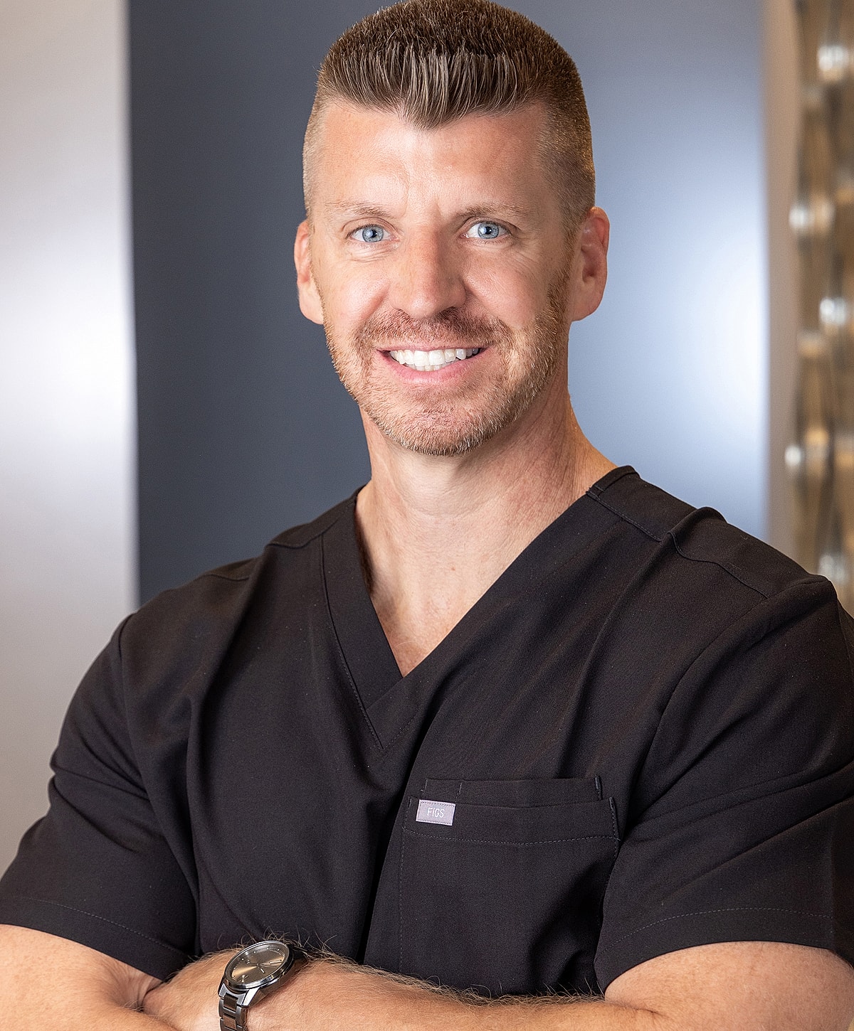 Smiling professional in black scrubs with arms crossed.